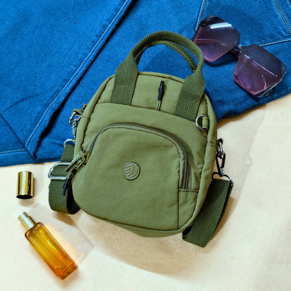 Green bag with sunglasses and a bottle on a blue fabric background