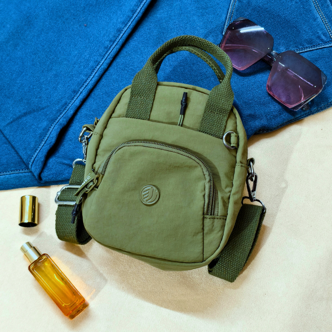 Green bag with sunglasses and a bottle on a blue fabric background