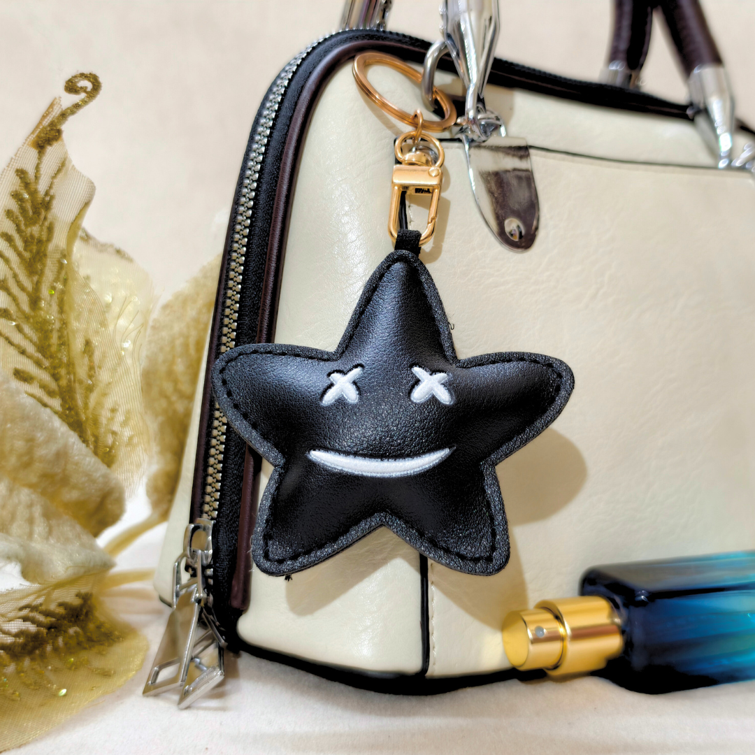 Black star-shaped keychain with white accents on a beige handbag.