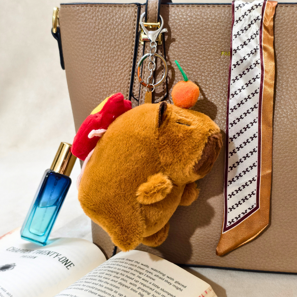 Plush keychain attached to a handbag with a book and perfume bottle in the foreground