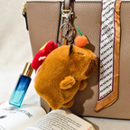 Plush keychain attached to a handbag with a book and perfume bottle in the foreground