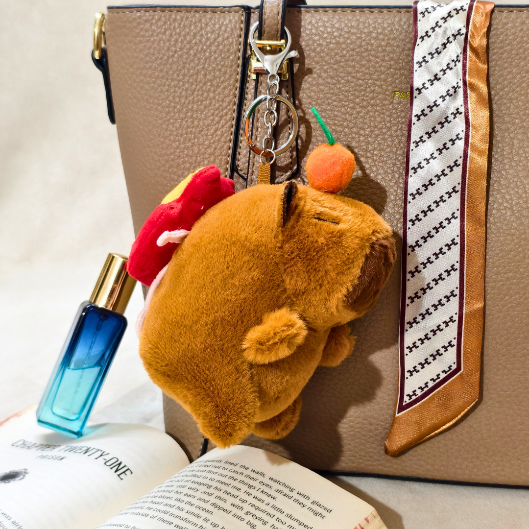 Plush keychain attached to a handbag with a book and perfume bottle in the foreground