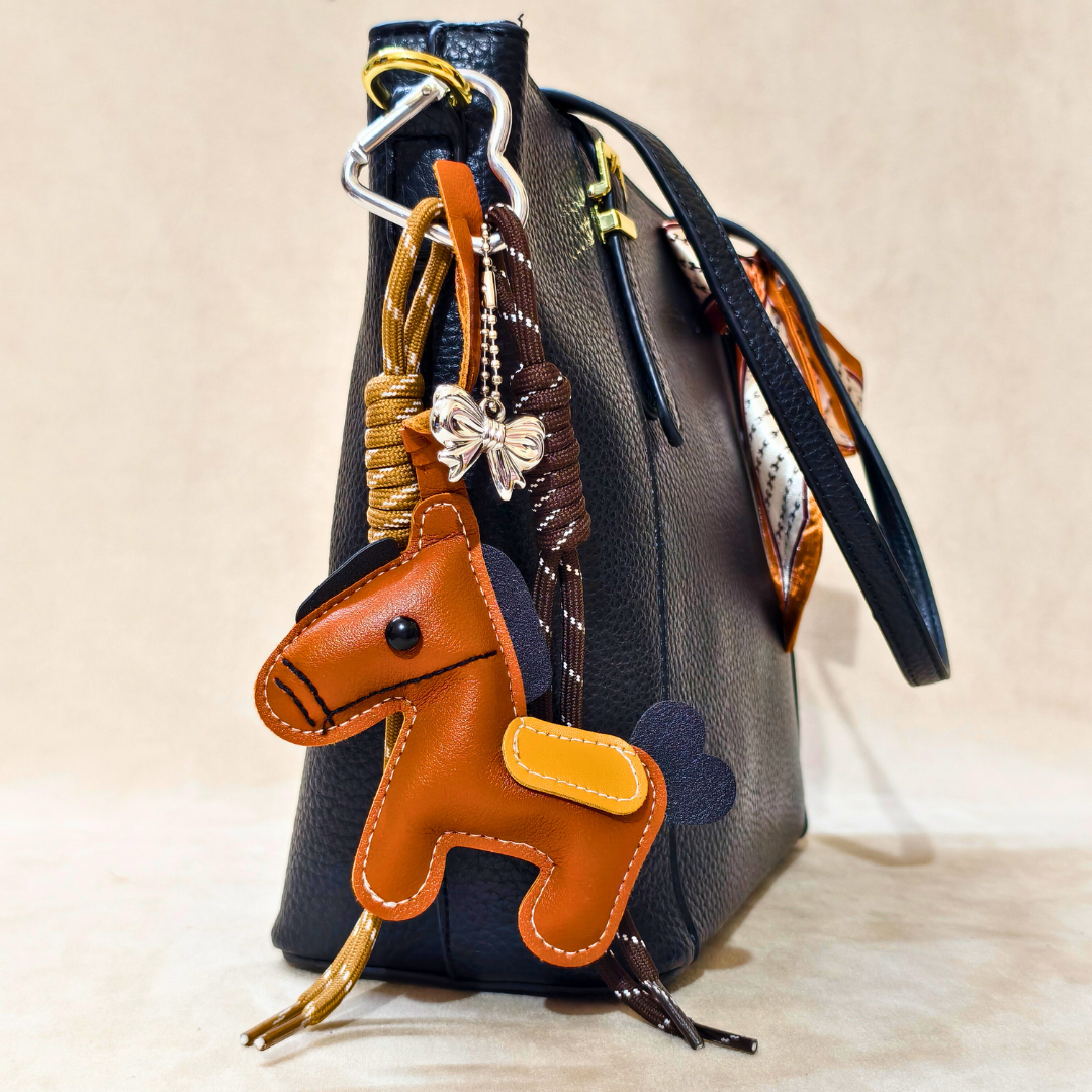 Brown leather horse keychain attached to a gray handbag with a beige background