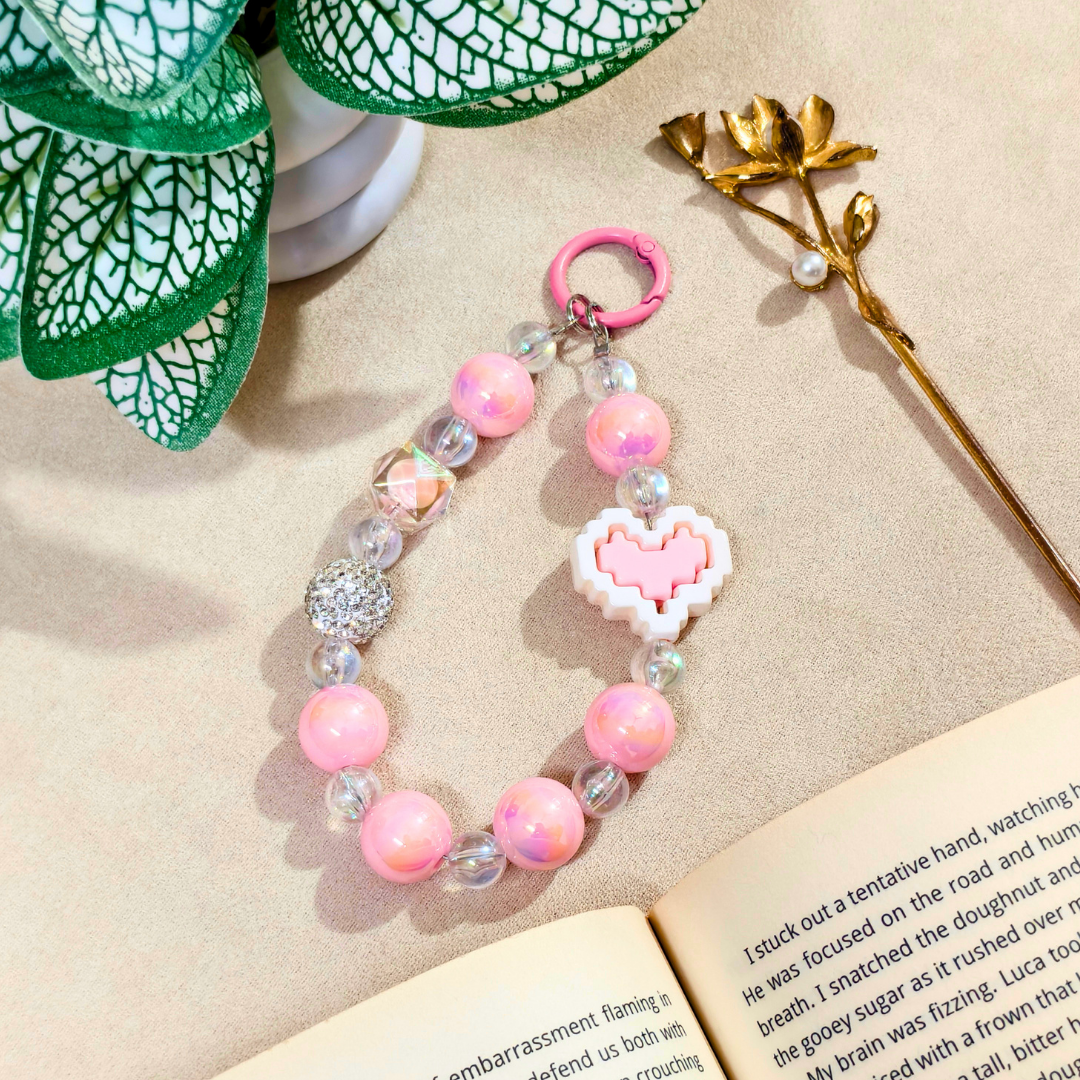Pink beaded keychain with heart charm on a book next to green leaves and gold flower