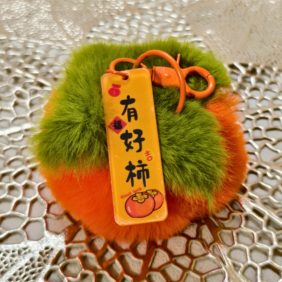 Fluffy orange and green keychain with a yellow tag on a textured surface