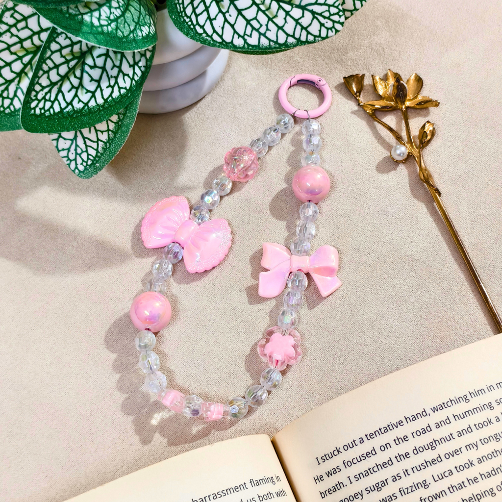 Pink beaded bracelet with bow decorations on a beige surface with a book and plant in the background