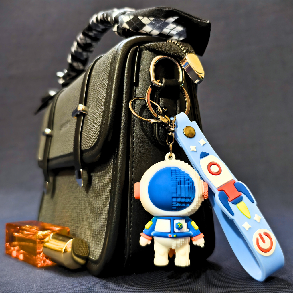 Black handbag with keychain featuring an astronaut and rocket design on a dark background