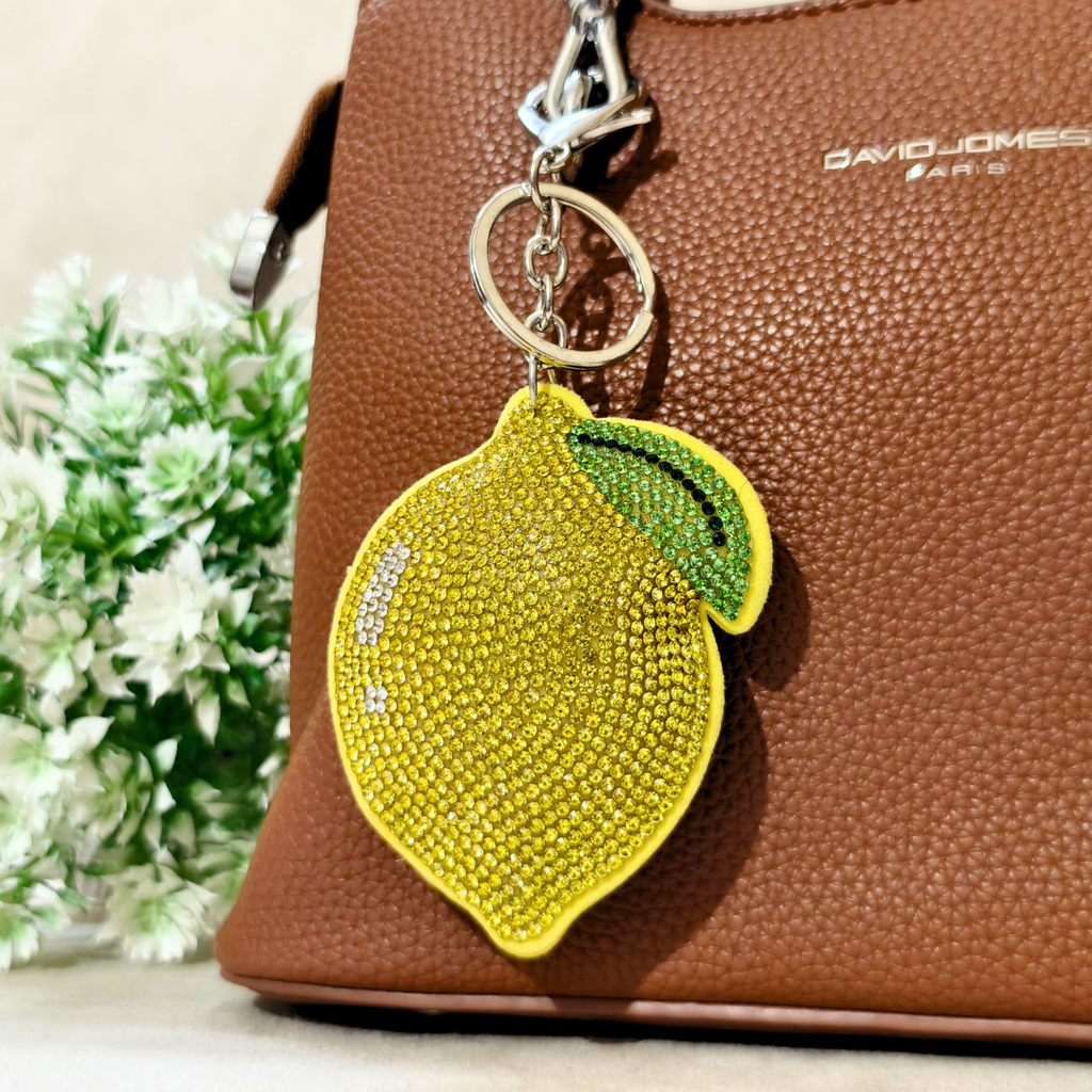 Lemon-shaped keychain with rhinestones on a brown handbag with 'David Jones' branding.