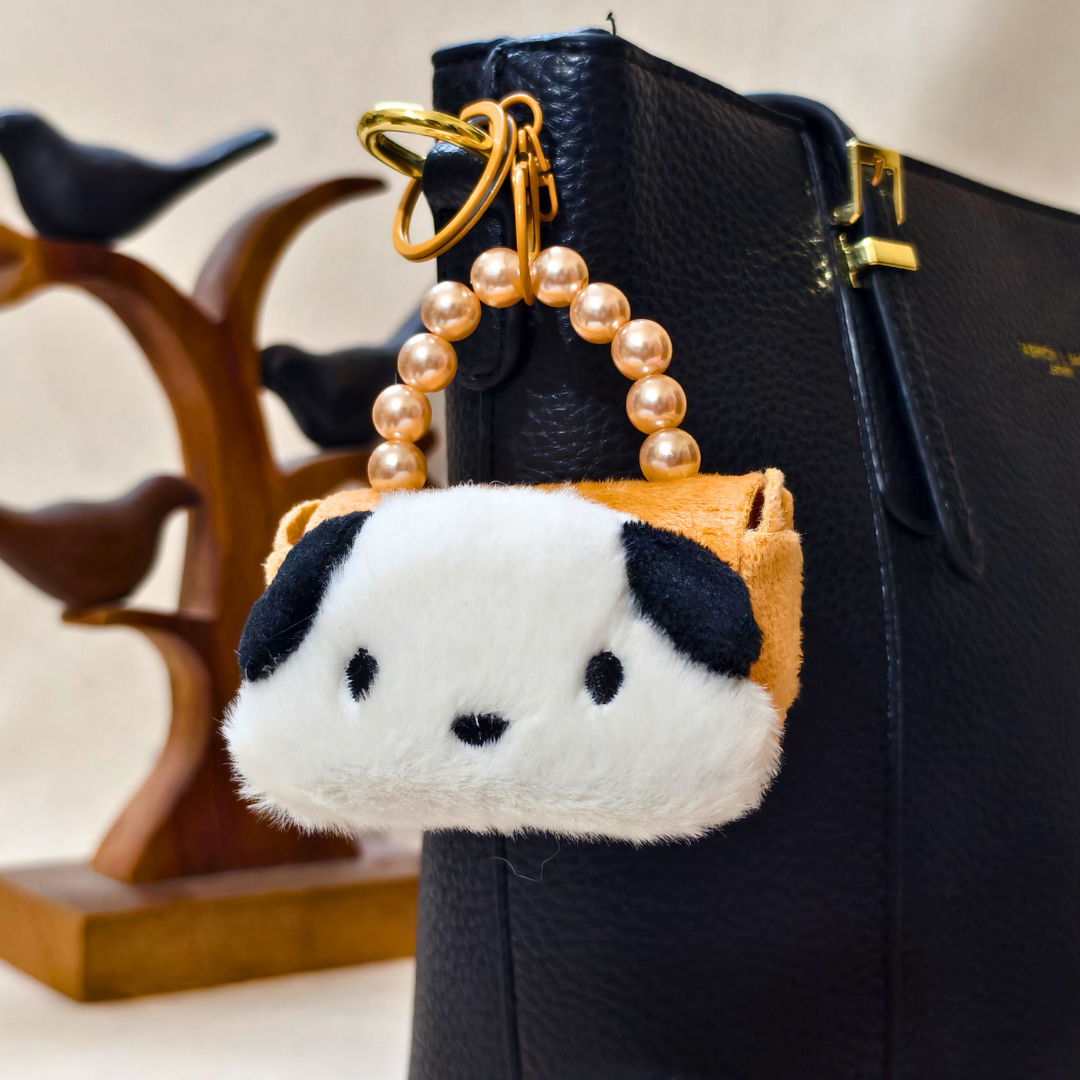 Plush keychain shaped like a panda with a pearl handle attached to a black handbag.