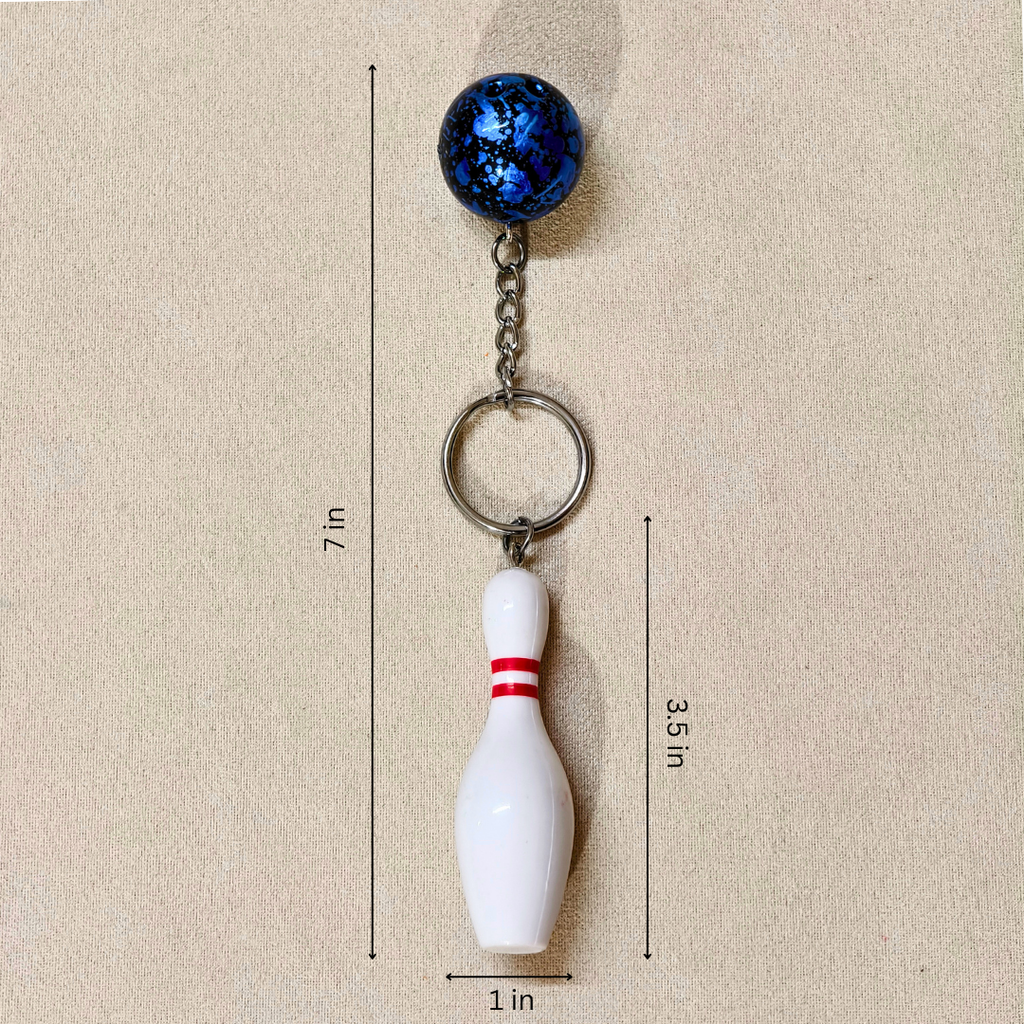 A bowling pin keychain with a blue marbled ball charm, metal chain, and white bowling pin charm with red stripes, shown on a beige background with height and width measurement lines and labels.