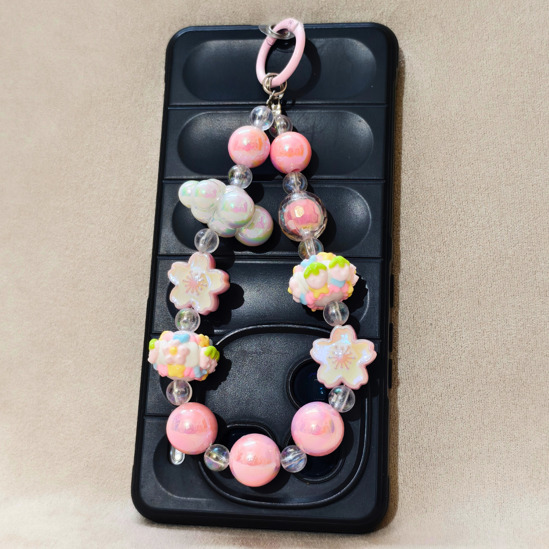 Decorative keychain with pink beads and floral designs on a black phone case.