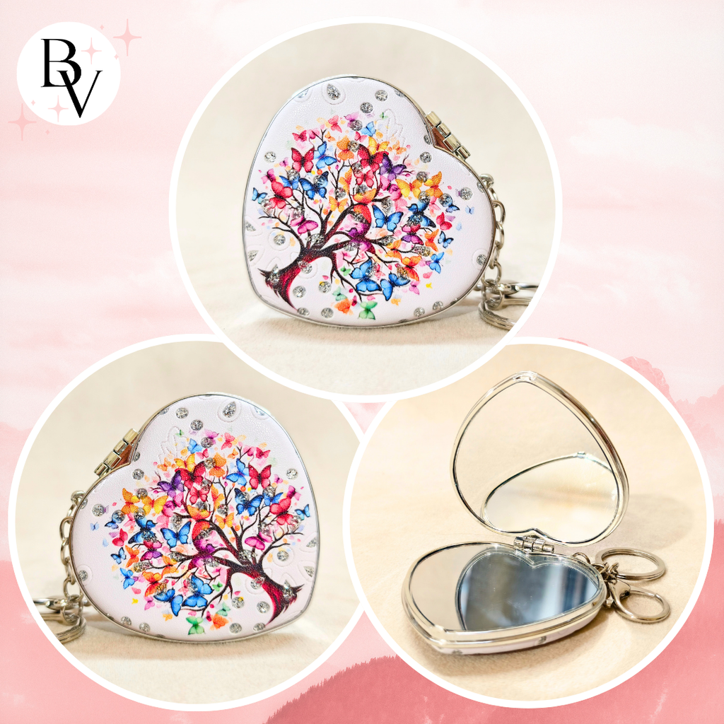 Heart-shaped silver compact mirror with a colorful butterfly tree design, shown closed and open on a soft pink background.