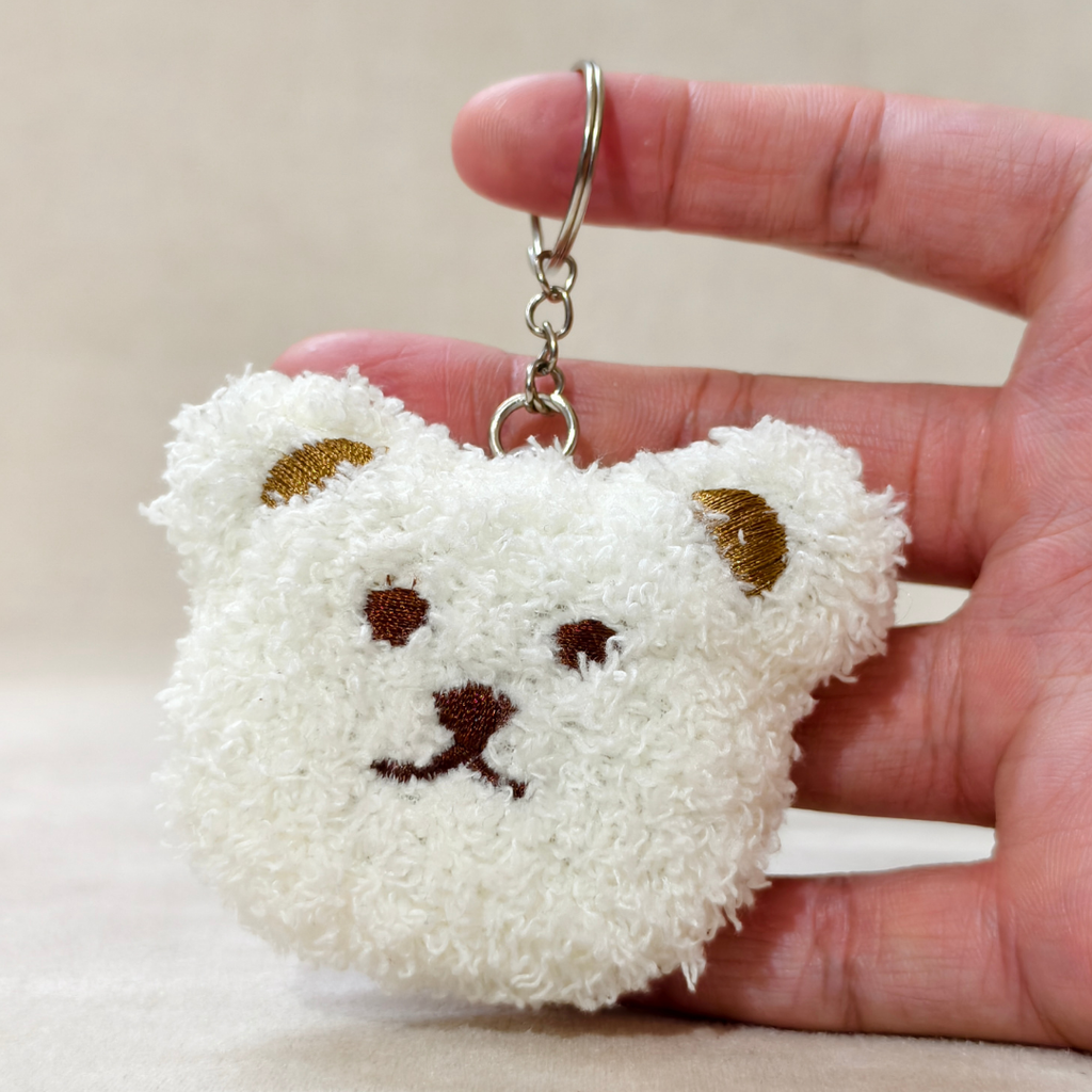 A white fluffy teddy bear face charm with brown ears, nose, and eyes, hanging from a silver-tone ring hand carry,