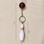 A bowling pin keychain shown on a beige textured background with dimension lines and labels indicating a height of 7 inches, pin height of 3.5 inches, and pin width of 1 inch.