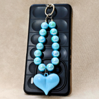 Blue beaded keychain with a heart pendant on a black phone case.