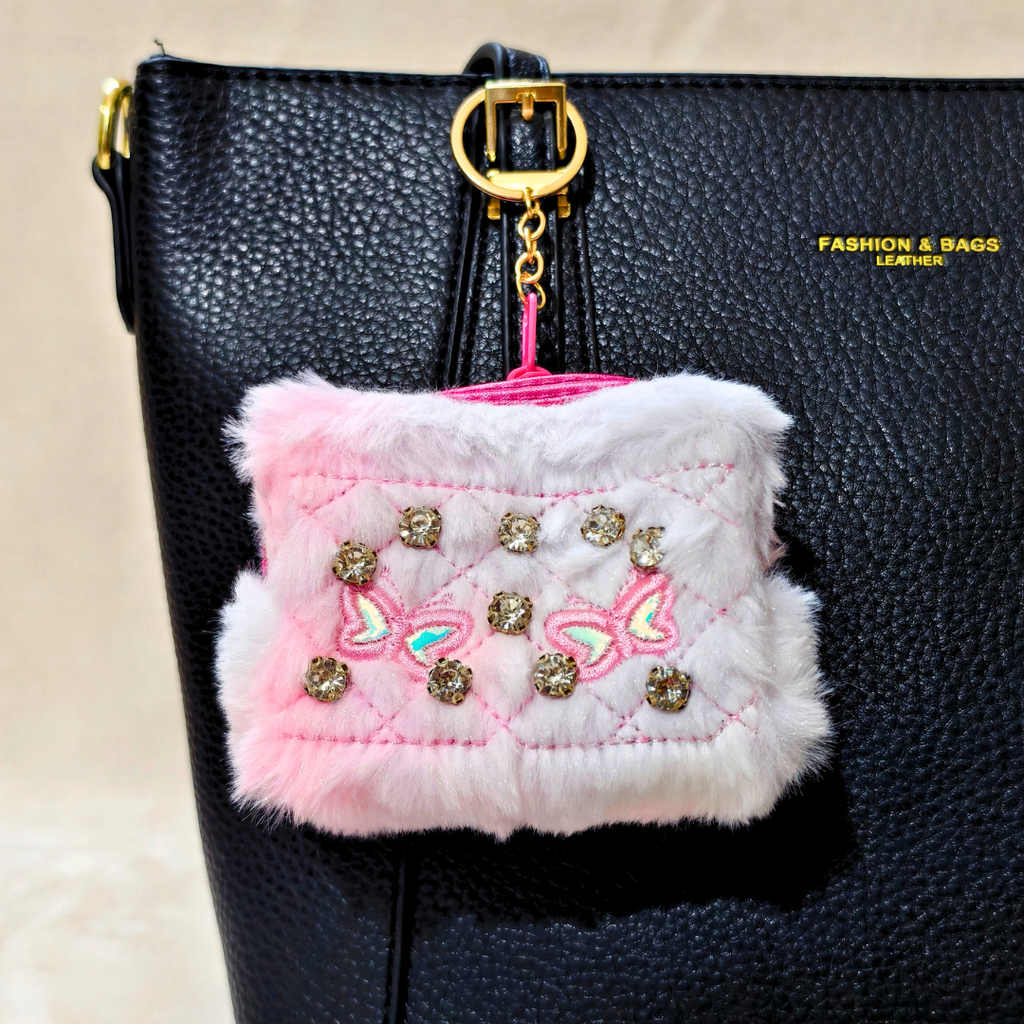 Pink fluffy pouch with decorative elements attached to a black bag.