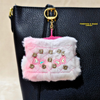 Pink fluffy pouch with decorative elements attached to a black bag.