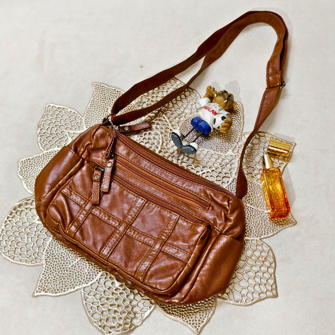 Brown leather handbag on a textured surface with a small toy and perfume bottle.