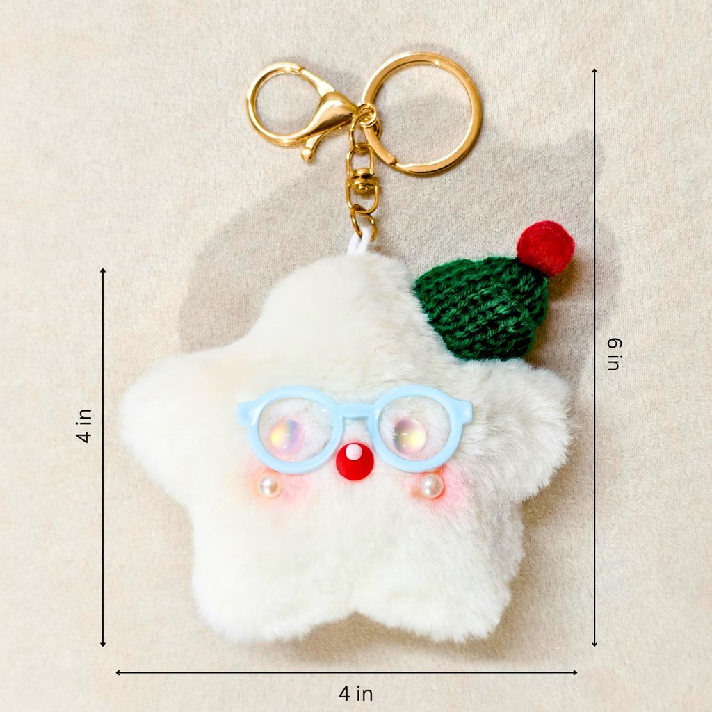 A fluffy white star-shaped keychain charm with light blue glasses, a red nose, and a green knit hat with a red pom-pom, shown on a beige background with black dimension lines and text indicating 4 in by 6 in measurements.