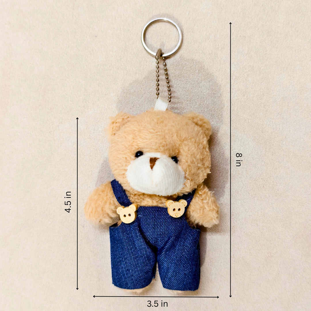 Teddy bear keychain with denim overalls and measurements on a beige background