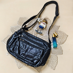Black leather handbag with decorative charm and perfume bottle on a textured beige surface