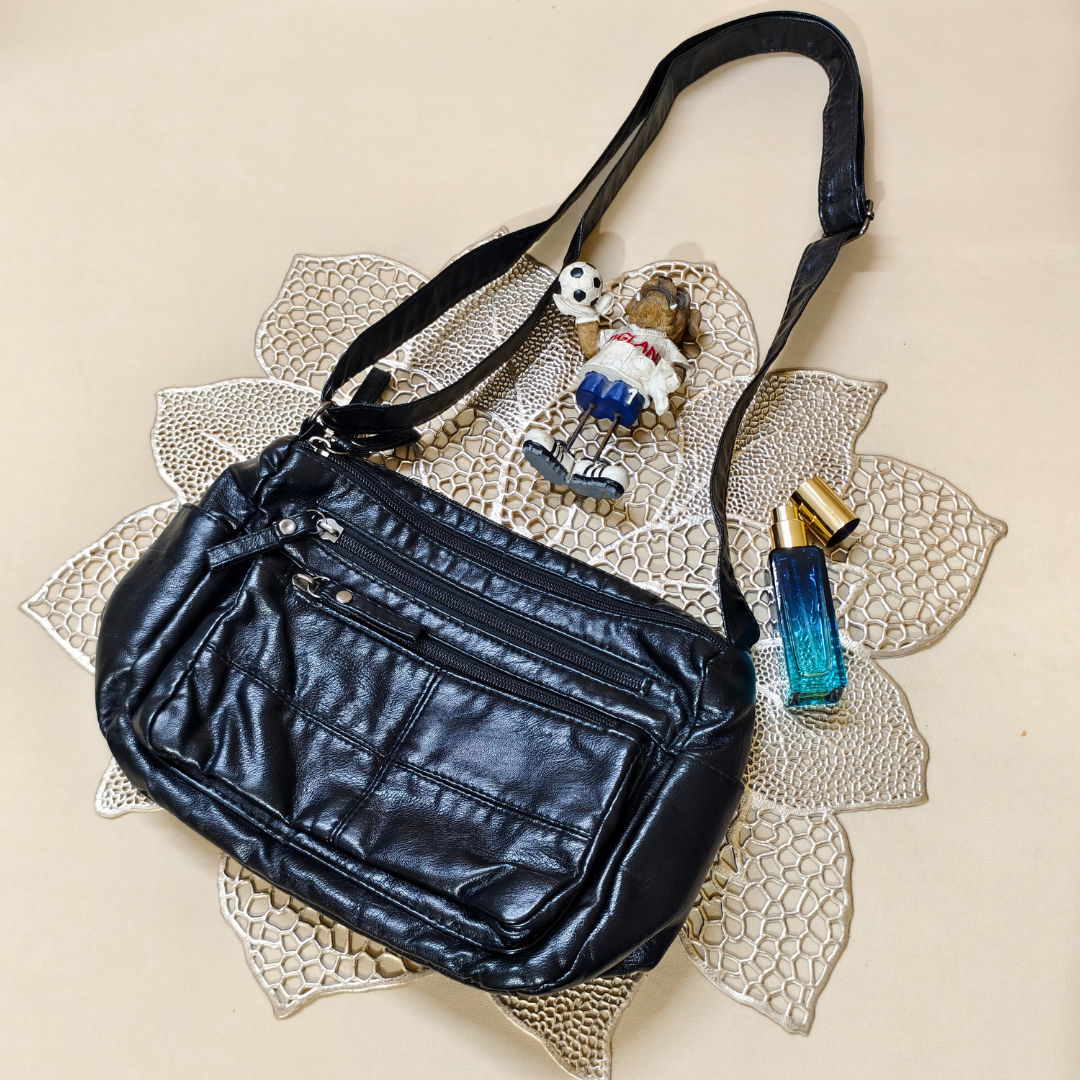 Black leather handbag with decorative charm and perfume bottle on a textured beige surface