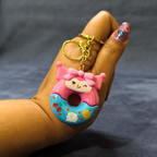 Hand holding a colorful keychain shaped like a donut with a character on a dark background