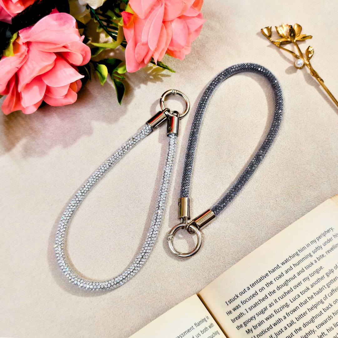 Gray braided lanyard with metal clip on a textured surface with pink flowers and an open book.