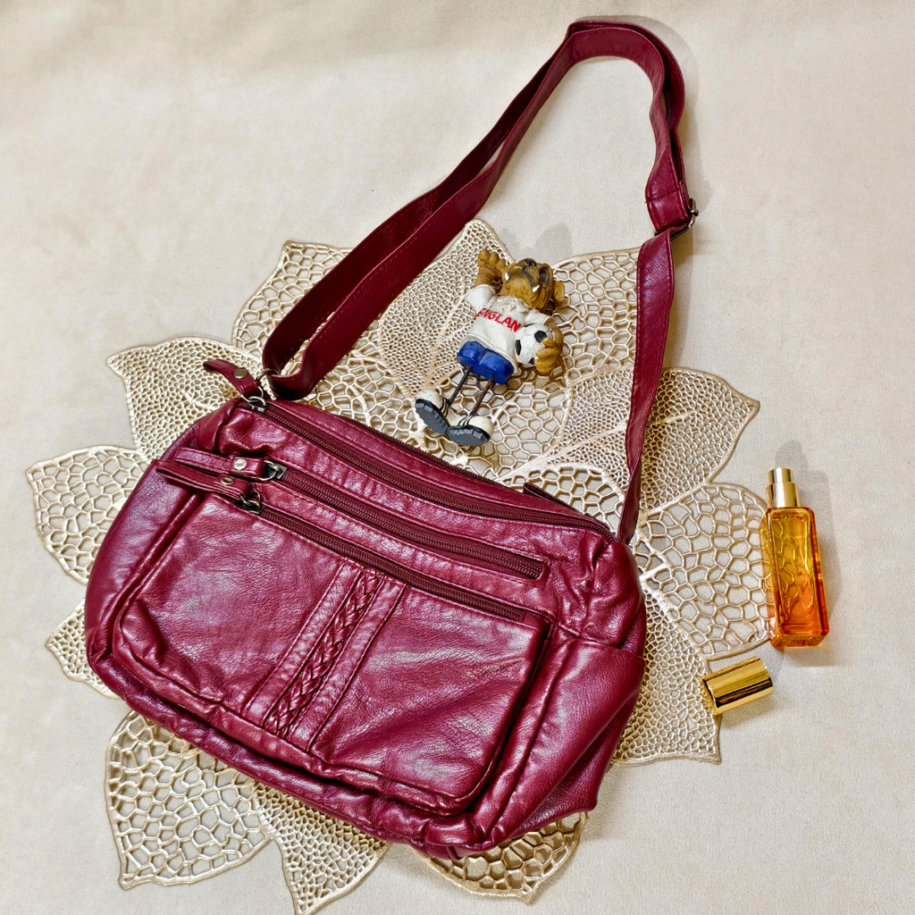 Red leather bag with a small bear figurine and perfume bottle on a textured surface