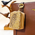Gold leopard print pouch attached to a brown leather handbag with a blurred background