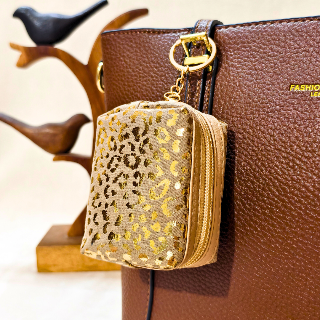 Gold leopard print pouch attached to a brown leather handbag with a blurred background