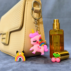 Pink unicorn keychain with rainbow on a beige handbag next to a gold bottle.