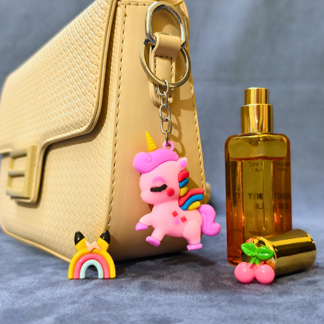 Pink unicorn keychain with rainbow on a beige handbag next to a gold bottle.