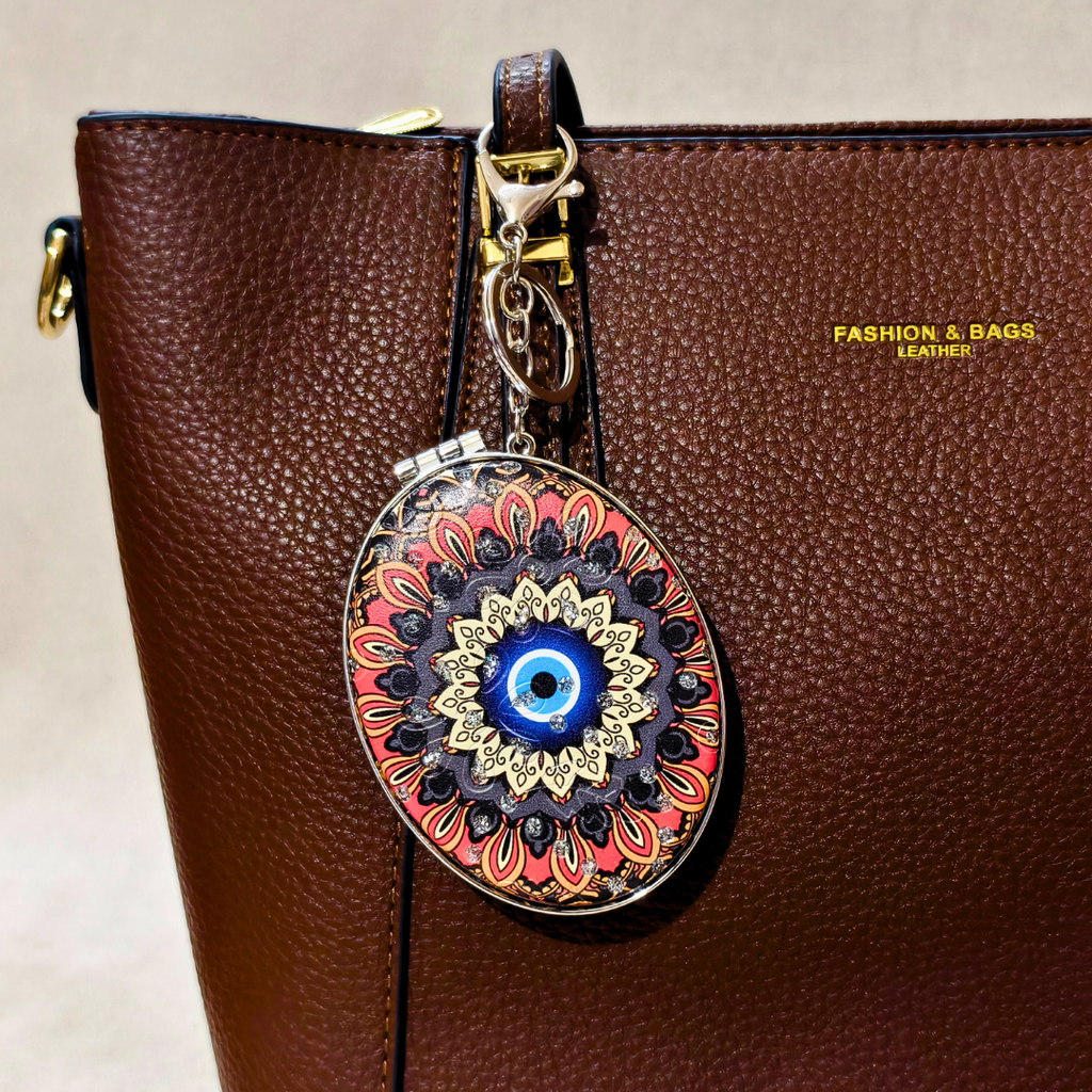 
Oval Evil Eye Black Pocket Mirror Attached With Purse As  Bag Charm On  Beige Background.