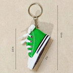 A miniature green canvas high-top sneaker keychain with white laces and a white rubber toe cap, shown on a beige textured background with dimension lines and measurements.