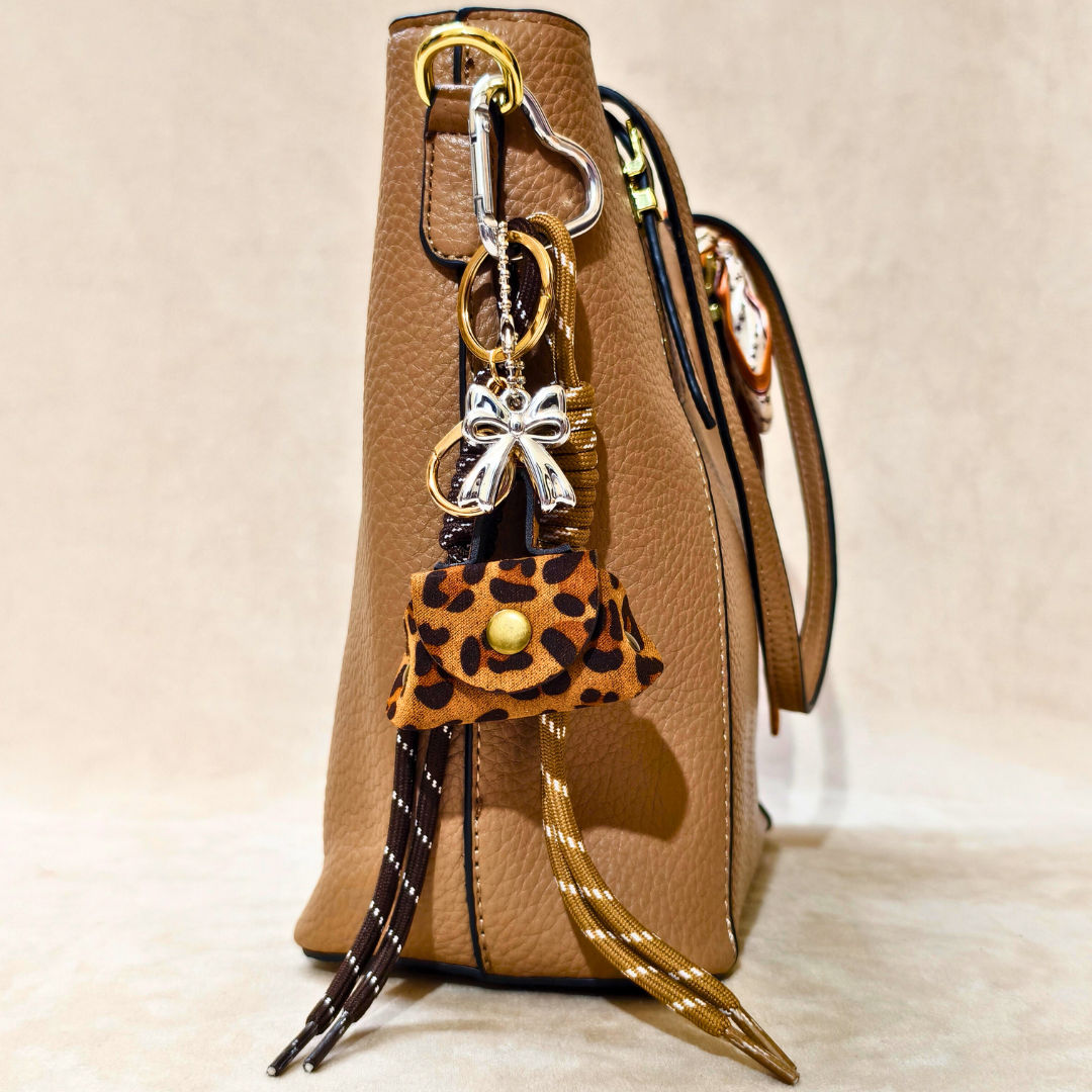 Leopard print keychain with bow charm attached to a brown handbag on a beige background