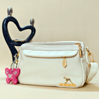 White handbag with gold accents and a pink butterfly keychain on a beige background