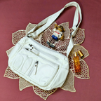 White handbag with accessories on a decorative mat with a pink background
