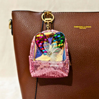Pink sequined backpack charm with colorful heart design on a brown leather bag.