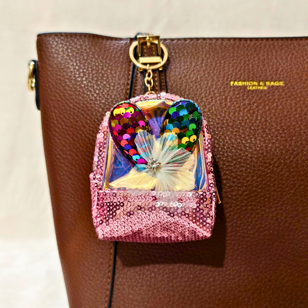 Pink sequined backpack charm with colorful heart design on a brown leather bag.