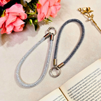 Gray braided lanyard with metal clip on a textured surface with pink flowers and an open book.