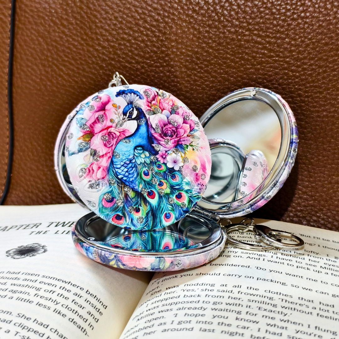 Compact mirror with peacock design on a book