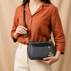Person holding a black handbag with a visible brand logo against a beige background