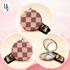 A round compact mirror with a pink and dark brown checkerboard patterned cover, shown in three views: closed, closed with a black ribbon, and open with the mirror side visible. A 'BV' logo is in the top left corner.