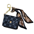 Black patterned purse charm with gold chain and beige scarf on a white background