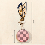 A small round coin purse keychain with a pink and gray checkerboard pattern, attached to a gold and navy ribbon with metal key rings. Black dimension lines and text indicate a height of 9.