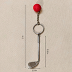 A golf club-shaped keychain with a red textured ball on top, shown on a beige background with dimension lines and labels indicating 7 in total height, 3.5 in shaft height, and 1.