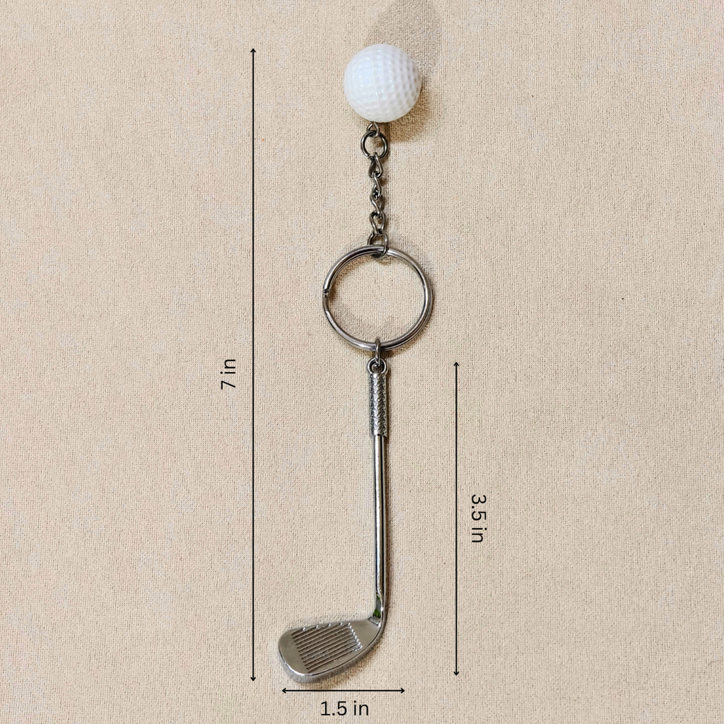 A golf-themed keychain featuring a miniature golf club head, a silver split ring, a short chain, and a white golf ball on top, shown with dimension lines indicating a height of 7 in, club head width of 1.5 in, and club head length of 3.