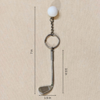 A golf-themed keychain featuring a miniature golf club head, a silver split ring, a short chain, and a white golf ball on top, shown with dimension lines indicating a height of 7 in, club head width of 1.5 in, and club head length of 3.