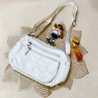 White crossbody bag with a keychain and bottle on a decorative mat